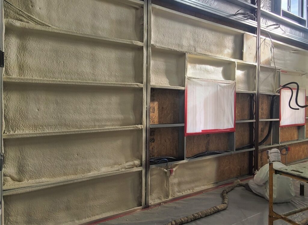 Female technician applying spray foam insulation between steel studs in a custom home under construction in Kawartha Lakes.