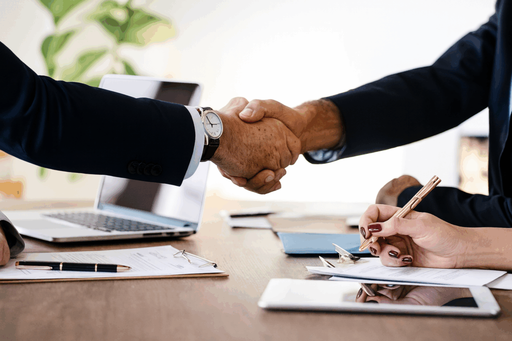 Professional business handshake between client and Custom Home Builders in Calgary, ConstructionX, over architectural planning documents.